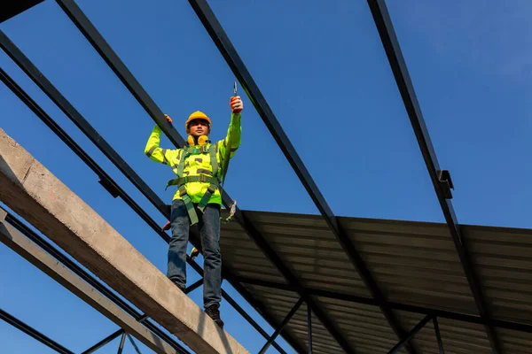 Asian worker wear safety height equipment to install the roof in the construction site;. Fall arrestor device for worker with hooks for safety body harness.