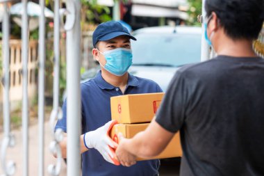 Tıbbi lastik eldivenler ve maske içinde karton kutular taşıyan Asyalı bir adam. Çevrimiçi alışveriş ve ekspres teslimat ya da ecommerce. Mikropların yayılmasını önler ve enfeksiyonları önler Covid-19