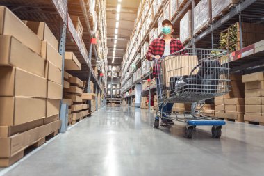Asyalı bir adam raflarda alışveriş maskesi takıyor. Evi dekore etmek için fabrika deposundaki modern sanayi deposunda malzeme kutularıyla birlikte.