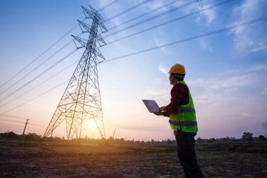 Elektrik mühendisi, inşaat alanındaki yüksek voltaj elektrik direklerinde elektrik üreterek planlama çalışmalarını izlemek üzere elektrik santralinde duruyor ve izliyor.
