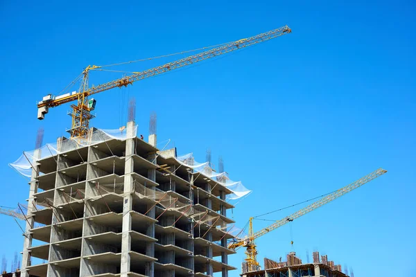 Building and cranes under construction. High-rise building under construction. Apartment building under construction and cranes against the blue sky.