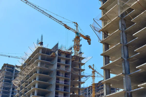 Building and cranes under construction. High-rise building under construction. Apartment building under construction and cranes against the blue sky.