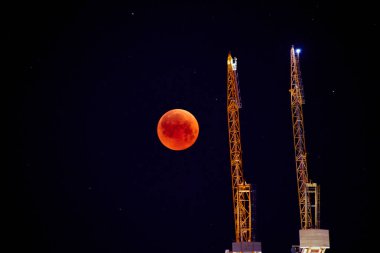 Tam kırmızı ay arka plan üzerinde inşaat vinç. Kırmızı ay, ay tutulması. Karanlık gece gökyüzüne bir toplam ay tutulması.