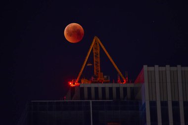 Tam kırmızı ay arka plan üzerinde inşaat vinç. Kırmızı ay, ay tutulması. Karanlık gece gökyüzüne bir toplam ay tutulması.