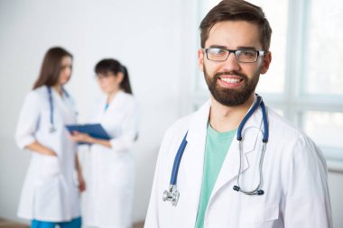 Arka planda meslektaşları olan genç bir doktorun portresi.