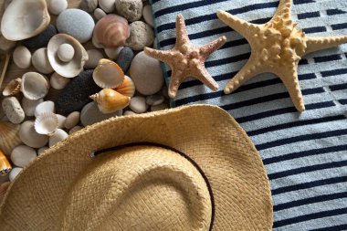 Yaz, deniz taşları, deniz kabukları, şapka ve plaj havlusuyla dolu.