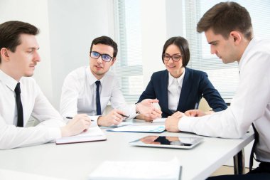 Genç iş adamları ofiste bir toplantıda masanın etrafında oturuyorlar.