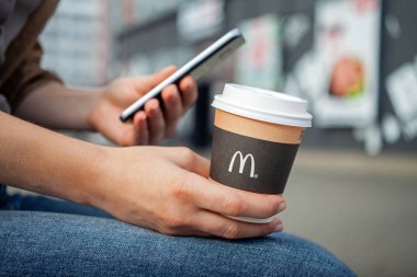 Minsk, Beyaz Rusya, 02 Temmuz 2019: Mcdonald's logolu kağıt bardak tutan eller akıllı telefon kullanıyor