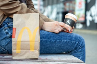 Minsk, Beyaz Rusya, 02 Temmuz 2019: Kağıt torba Mcdonald's elinde Mcdonald's logosu ile elinde kahve bir kadının yanında bir bankta Mcdonald's