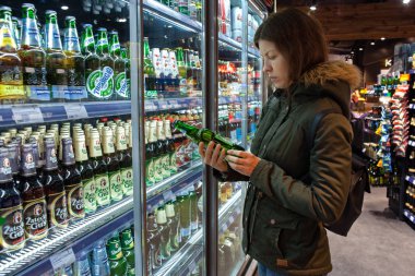 MINSK, BELARUS - 4 Ekim 2019: Kadın bakkaldan alkol alır. İçindekileri, bildirgeyi ya da son kullanma tarihini satın almadan önce okuyan genç bir kadın..