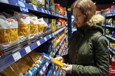 Minsk, Belarus - 4 Ekim 2019: alışveriş yapan kişi bakkaldan makarna seçiyor. Malzemeleri, beyanı ya da ürün üzerindeki son kullanma tarihini okuyan genç bir kadın satın almadan önce.