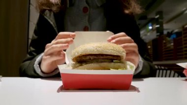 McDonald 's restoranının logosunun olduğu Big Mac kutusu. Big Mac 'le eller açık, kadın hamburgeri alıyor ve yiyor. Minsk, Belarus - 8 Ağustos 2020.