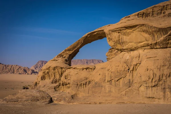 Büyük delikli bir dağ ile kayalık bir çöl görüntüsü.
