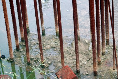 Etrafında su ve çimen olan beton çelik çubuklu bina inşaatı.