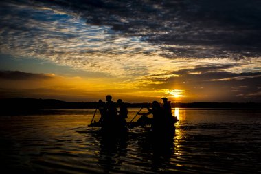 Bir grup insan, gün batımını takip ederek denizde yüzüyorlar.