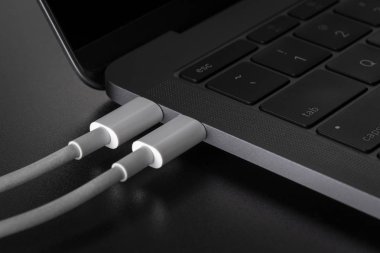 İki beyaz Usb tip C kablosu siyah arka plan üstünde laptop bağlı