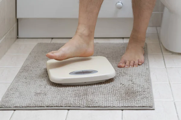 Cropped image of man feet stepping on weigh scales, on the bathroom floor