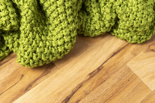 Wool blanket, green, knitted large chunky yarn. Close-up of knitted blanket on wooden background.