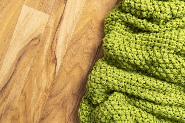 Wool blanket, green, knitted large chunky yarn. Close-up of knitted blanket on wooden background.