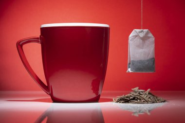Çay ve çay poşeti kırmızı zemin üzerine izole küçük yığını ile kırmızı kupa