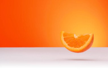 Floating piece of orange isolated on an orange and white background with space for text clipart