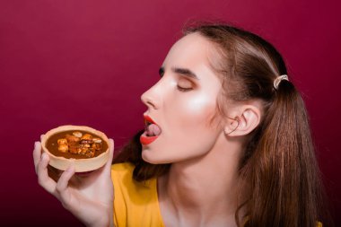 Neşeli esmer kız kırmızı dudaklı tart kek ile eğleniyor. Stüdyo vurdu