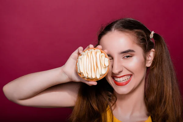 Pleased brunette girl with red lips having fun with caramel tart cake. Space for text