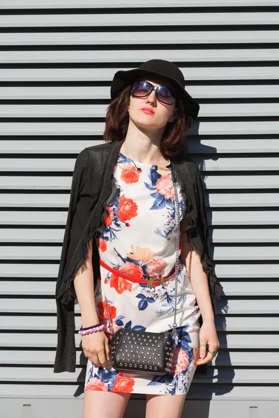 Attractive young model wearing hat and sunglasses, posing near the shutters in rays if sun