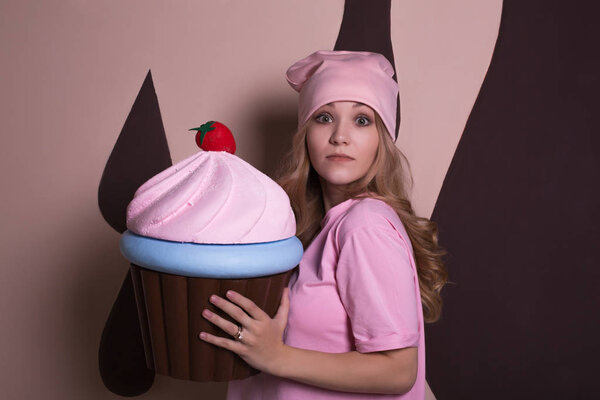 Surprised young blonde woman posing with big cupcake sweet decoration