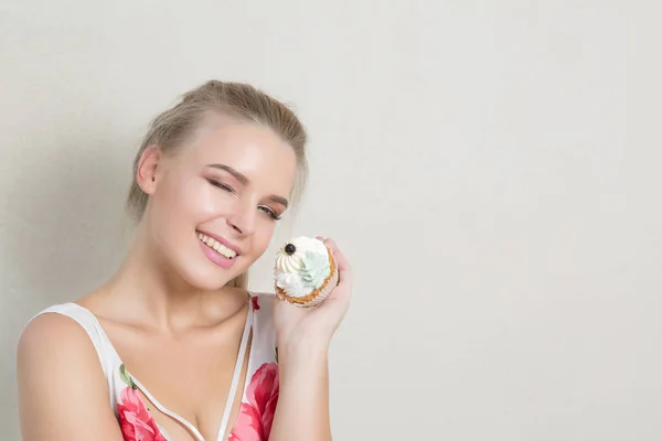 Cool winking blonde girl with perfect makeup holding sweet cream dessert. Empty space