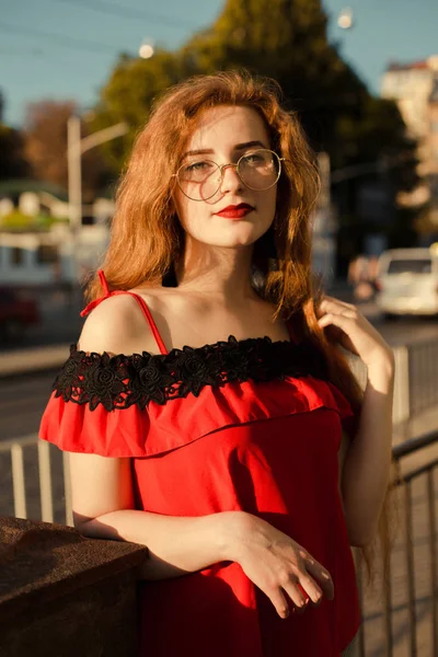 Portrait of stunning ginger woman with freckles wearing glasses, posing in soft sunlight