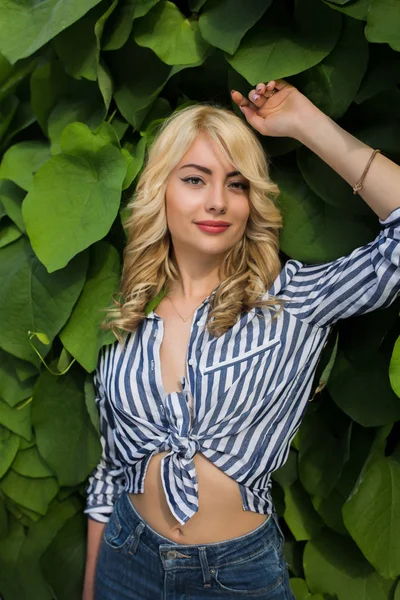 Mutlu genç modeli kıvırcık saçlı ve yeşil yaprakları arka plan poz mükemmel makyaj