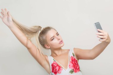 Saçlarını çekerek ve cep telefonu gri bir arka plan selfie yapma sihir sarışın kadın
