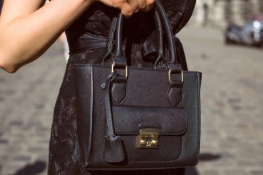 Şehir arka plan siyah deri çanta tutan el. Closeup çekim