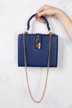Mavi deri çanta altın zinciri ile beyaz bir arka plan üzerinde tutan el