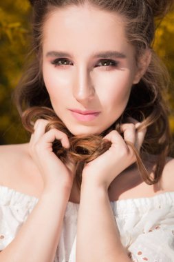 Portre portre şanlı esmer modeli duran sarı çiçek açan çiçekler güneş ışığında yakınındaki