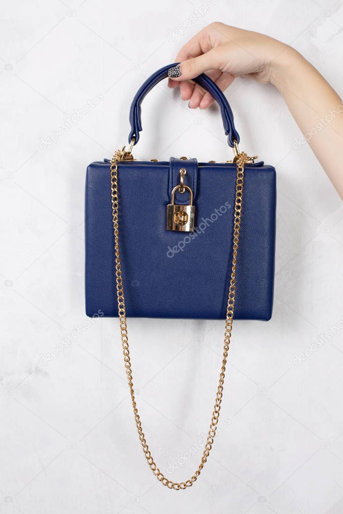 Female hand holding blue leather handbag with golden chain over a white background