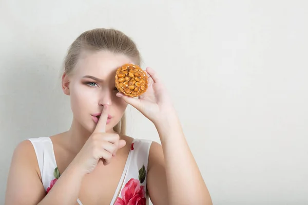 Attractive young girl covering eye with cupcake, showing silence gesture. Empty space