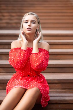 Kırmızı elbise giymiş, ahşap merdiven üzerinde poz çıplak omuz ile lüks sarışın model