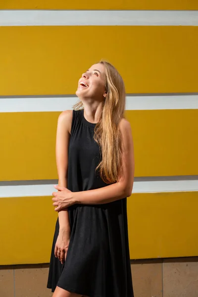 Veselá Blond Žena Černých Šatech Vystupují Proti Žluté Zdi — Stock fotografie