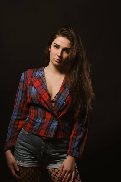 Fashionable brunette model with long hair posing in checkered jacket on a dark studio background with shadows