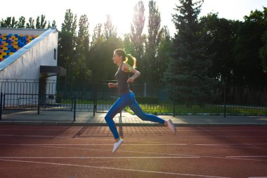 Gri t gömlek ve mavi tozluk güneşli gece boyunca stadyum yolda atlama oldukça sportif kadında. Metin için yer