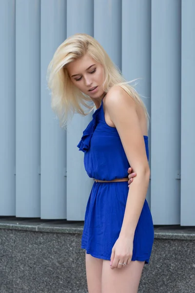 Attractive blonde woman in fashionable romper posing near the metal shutters at the city