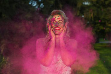 Holi festival kutluyor neşeli kafkas kadın kıvırcık saçlı pembe kuru boya, bulutu n ayakta