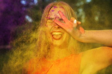 Neşeli sarışın kız sarı boya bulutu içinde Holi gösteren barış hareketi ayakta