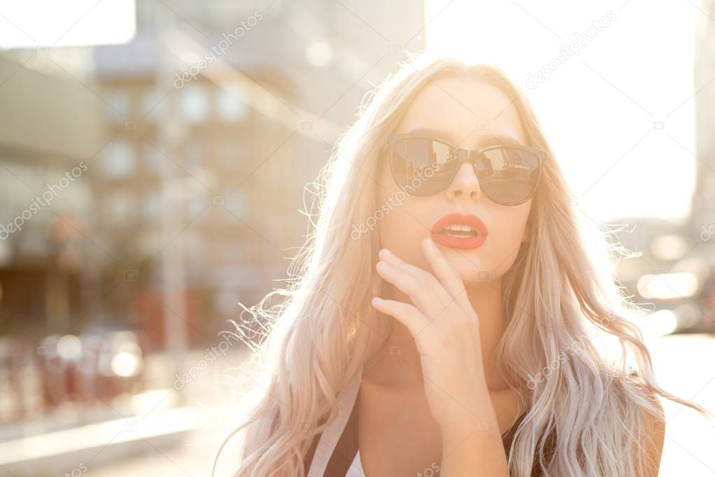 Closeup portrait of adorable blonde woman wearing glasses, walking at the city in sunny evening. Empty space