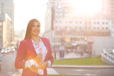 Bluz ve akşam şehir arka plan poz pembe ceket giyen mutlu esmer kadın. Boş alan