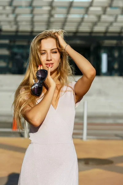 Mükemmel makyaj ile göz alıcı uzun saçlı kadın güneş gözlüğü, güneşli Caddesi'nde poz tutar