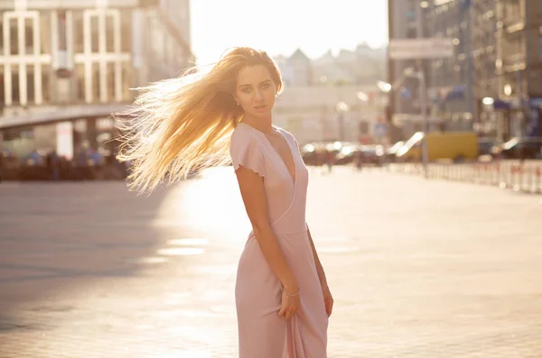 Luxury blonde model with flying hair posing at the street in sun beam. Female fashion concept. Empty space