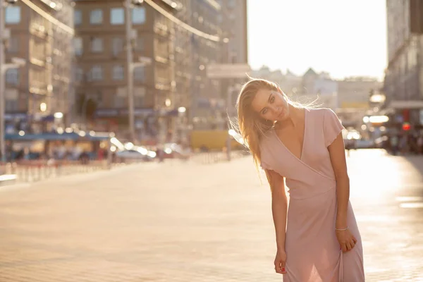 Stylish blonde girl with fluttering hair posing at the street in sun beam. Female fashion concept. Empty space